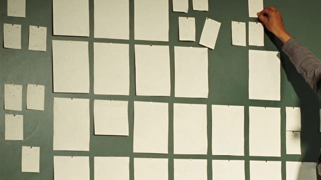壁一面に不揃いに貼られた無地の紙。右から伸びた腕が、そのうちの一枚を貼り直している