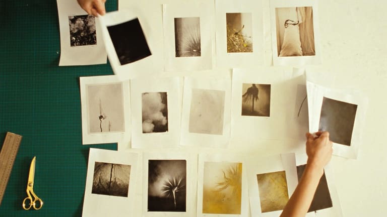 緑のカッターマットの上にセピア調の写真プリントを並べ替えている真上からの写真。両手が一枚ずつ位置を変えている