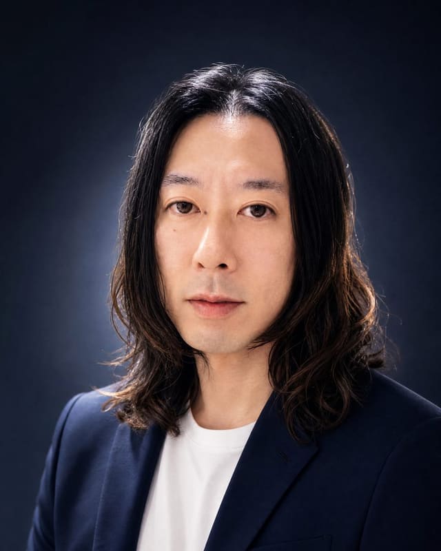 濃紺の背景の前で、ネイビーのジャケットに白いTシャツを合わせてこちらを見ている齊藤俊介